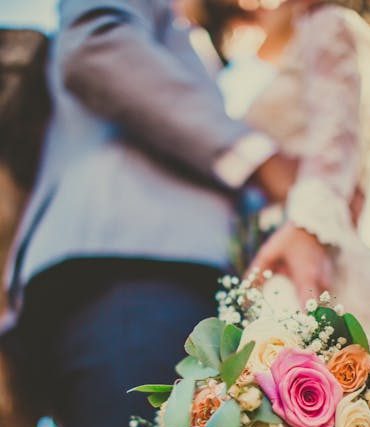 Close-up of a bride and groom embracing with a vibrant bouquet in focus, signifying love and celebration.